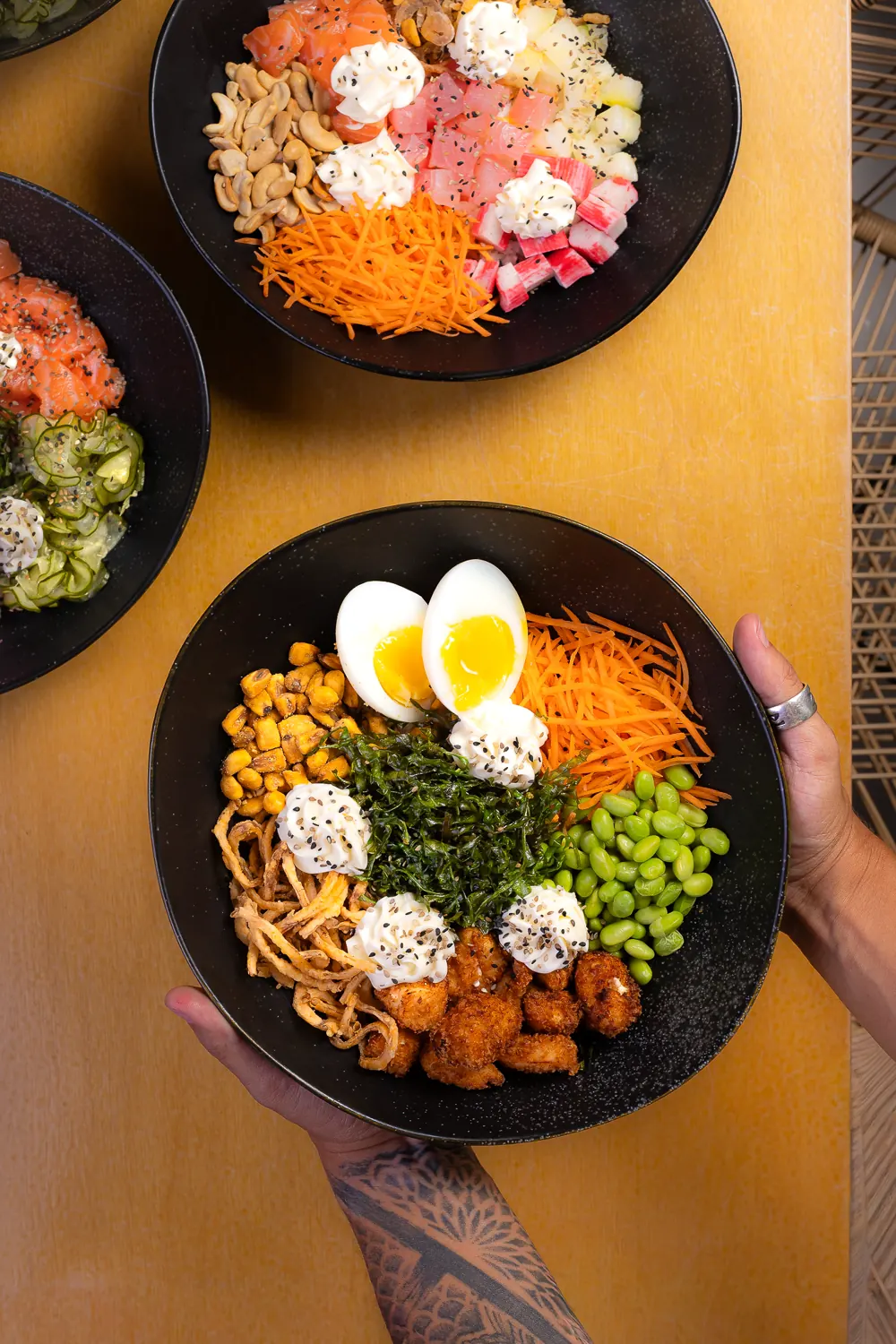 Mão segurando poke com frango, ovo, edamame e cenoura
